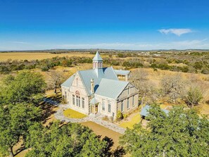 A stone church with a bell tower, surrounded by trees and open fields. - Morris Ranch Schoolhouse (Fredericksburg)
