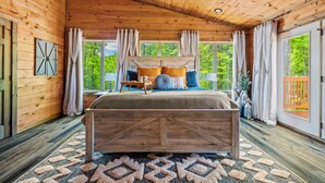 A wooden cabin bedroom with a large bed, windows, and a view of greenery. - Luxury Foliage Mtn Escape: Indoor Pool + Theater (Sevierville)