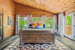 A wooden cabin bedroom with a large bed, windows, and a view of greenery. - Luxury Smoky Mtn Escape: Indoor Pool + Theater (Sevierville)