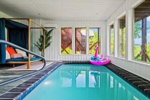 Zona de piscina con piso de baldosas azules y negras, un flotador inflable rosa y una silla colgante de madera.