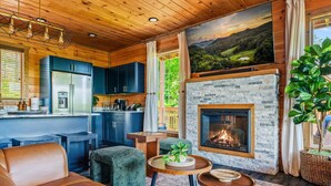 A cozy cabin interior with a stone fireplace, wooden ceiling, and a large window overlooking a scenic landscape. - Luxury Foliage Mtn Escape: Indoor Pool + Theater (Sevierville)