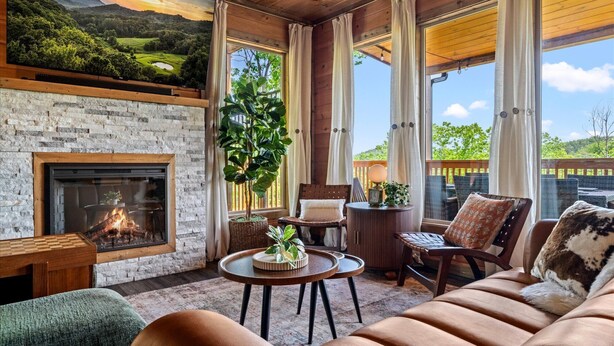 A cozy room with a fireplace, comfortable seating, a large window with curtains, and a view of greenery. - Luxury Foliage Mtn Escape: Indoor Pool + Theater (Sevierville)