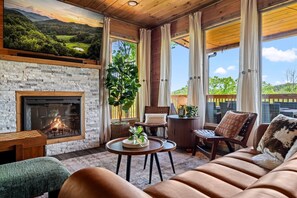 A cozy room with a fireplace, comfortable seating, a large window with curtains, and a view of greenery. - Luxury Foliage Mtn Escape: Indoor Pool + Theater (Sevierville)