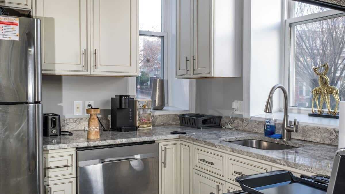 A modern kitchen with stainless steel appliances, white cabinetry, and a window with a view of trees.
