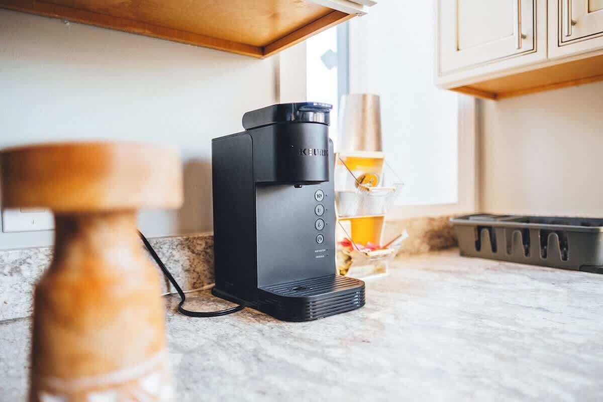 A coffee maker on a kitchen counter with a wooden spice jar and a glass container with a lemon slice.