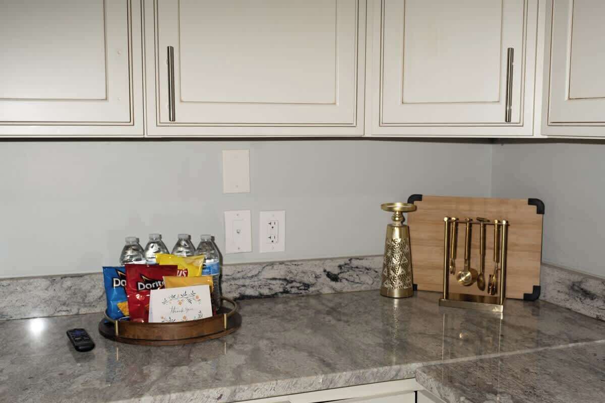 A kitchen with white cabinets, a marble countertop, and a fruit bowl with various snacks.