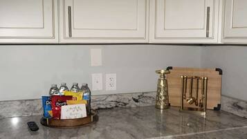 A kitchen with white cabinets, a marble countertop, and a fruit bowl with various snacks.