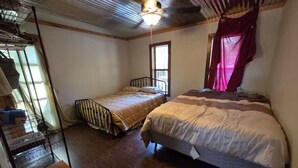 A small, cozy bedroom with two single beds, a wooden floor, a metal bunk bed, and a window with curtains.