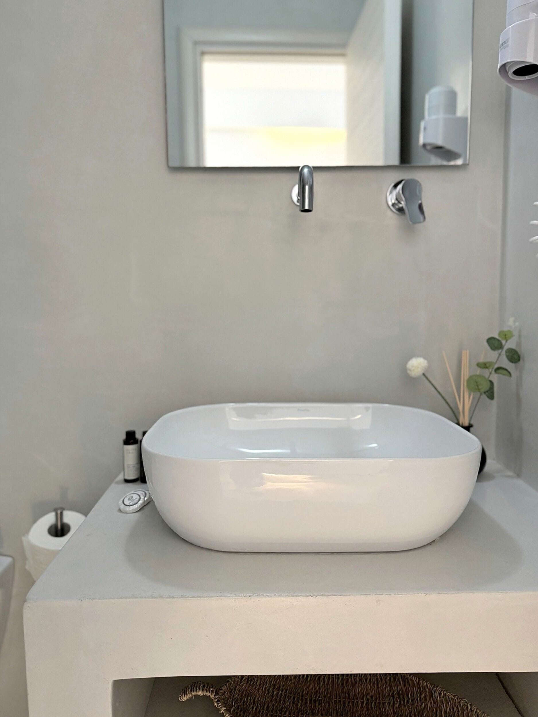 A white bathroom vanity with a large oval sink, a mirror above the sink, and a small plant on the right side.