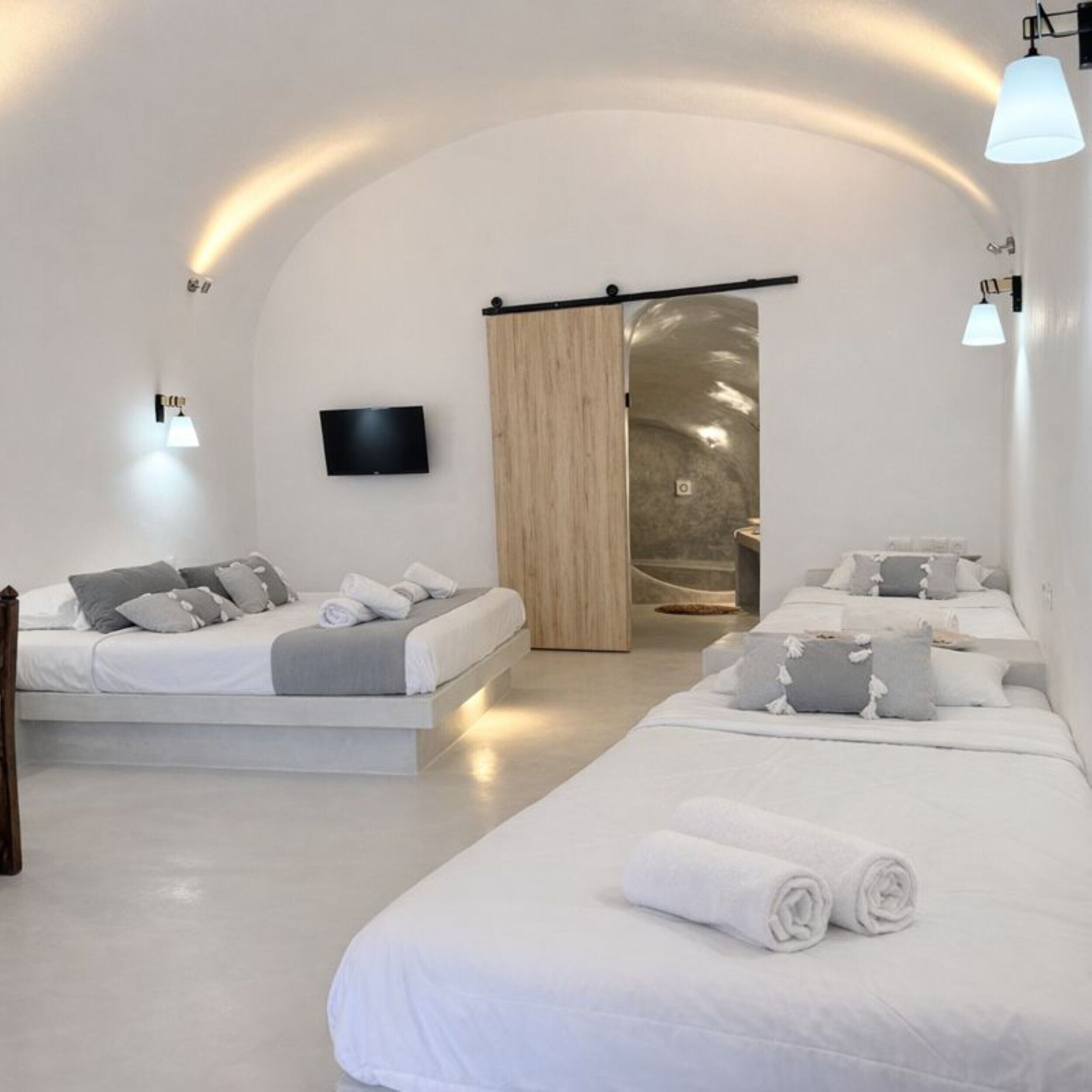 A modern, minimalist bedroom with two beds, a TV, and a sliding door leading to a bathroom.
