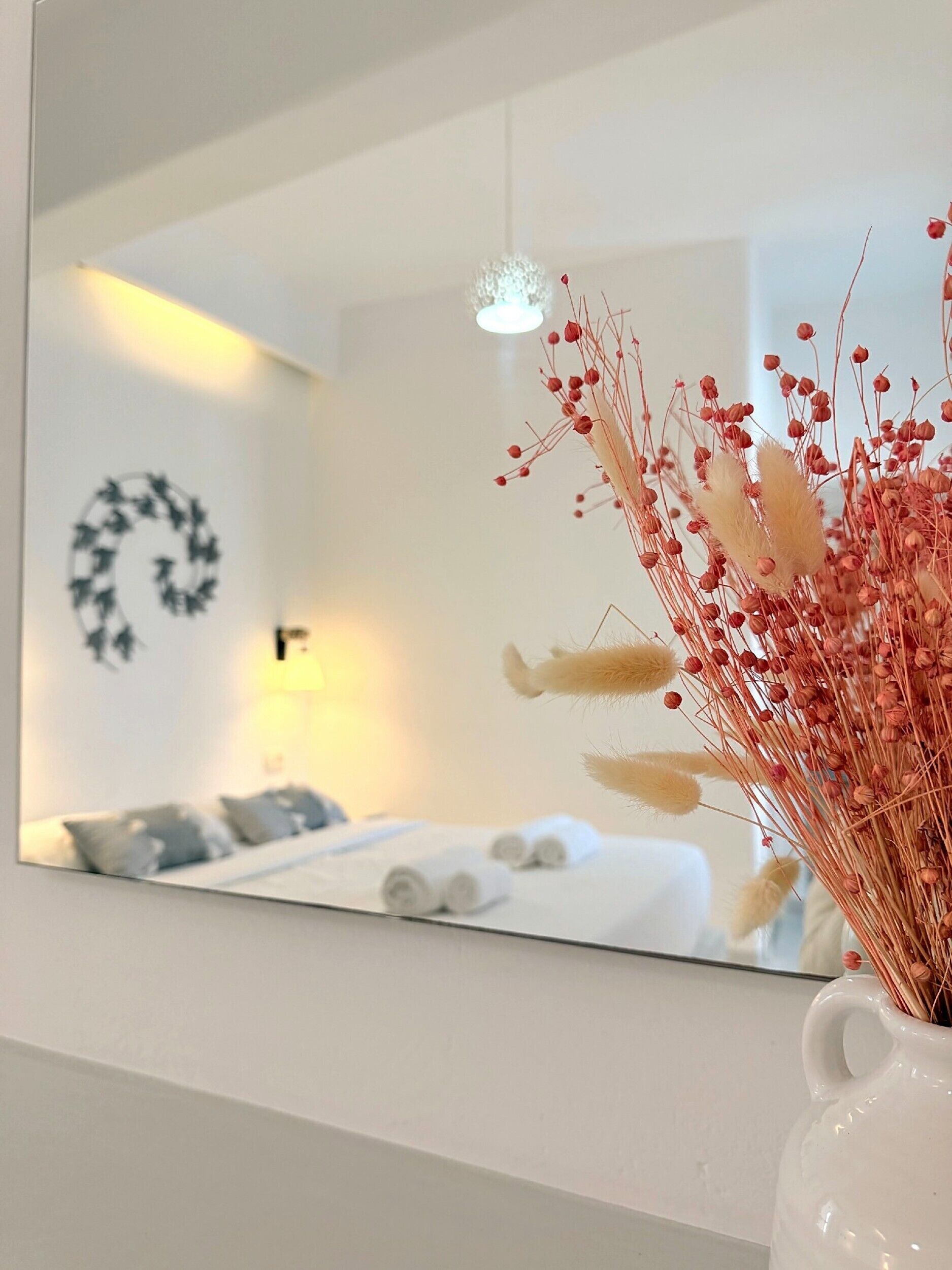 Un espejo refleja una habitación con una cama, una lámpara de pared y una guirnalda decorativa.