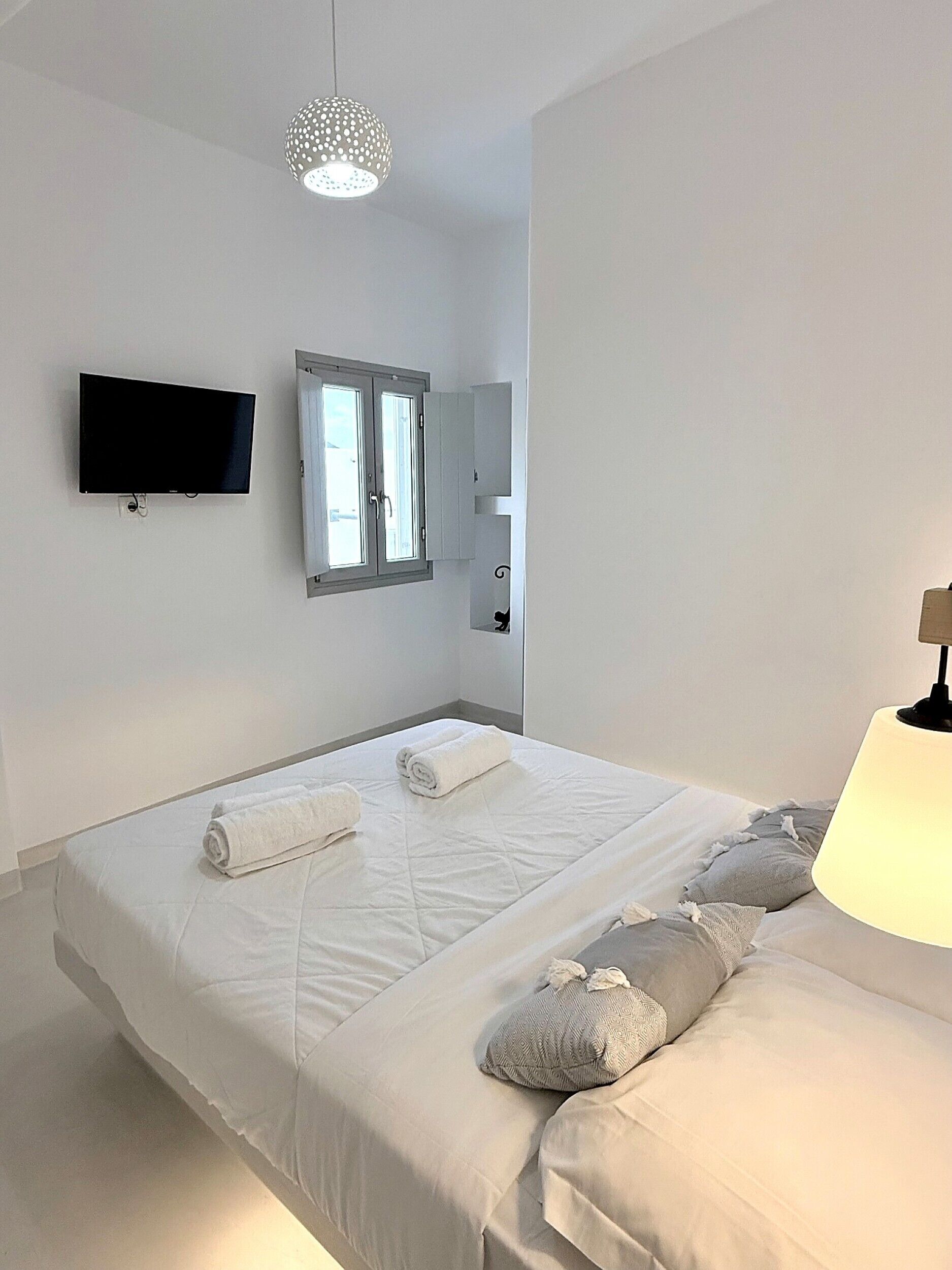 Un dormitorio moderno con una cama grande, un televisor de pantalla plana, una ventana con cortinas y una lámpara colgante.