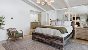 A bedroom with a large bed, a wooden headboard, a nightstand, a dresser, a mirror, and a chandelier. - Lakefront Luxury w/ Dock, Great Location! (Vinita)