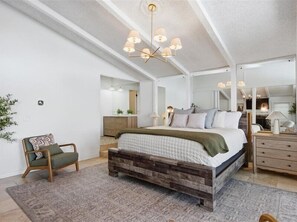 Un dormitorio con una cama grande, cabecera de madera, mesita de noche, cómoda, espejo y candelabro.