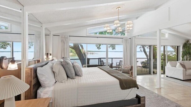 A spacious bedroom with a large bed, a view of the outdoors, and a balcony with seating. - Lakefront Luxury w/ Dock, Great Location! (Vinita)
