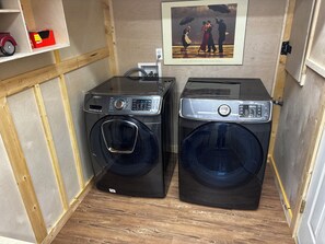 Une petite buanderie équipée de deux machines à laver à chargement frontal, d’une prise de courant et d’une œuvre d’art encadrée accrochée au mur.