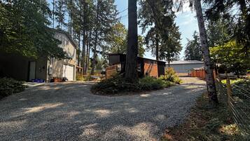 A gravel driveway leading to a building with a garage, surrounded by trees and a fenced area.