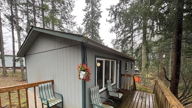 Une petite cabane dotée d’une terrasse, de deux chaises et d’un panier à fleurs suspendu.