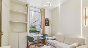 Ein modernes Wohnzimmer mit einer Couch, Sesseln, einem kleinen Tisch und einem Fenster mit Blick auf ein Gebäude.