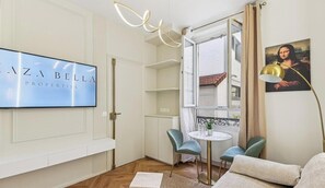 Ein modernes Wohnzimmer mit Flachbildfernseher, einem Essbereich mit kleinem Tisch und Stühlen sowie einem Balkon mit Aussicht.