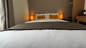 Une chambre d’hôtel comprenant un lit, deux lampes de chevet, une table de chevet en bois et une armoire.