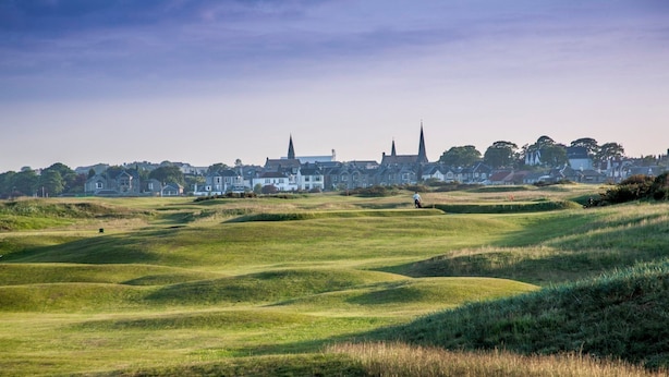 Un parcours de golf avec des collines verdoyantes et une ville en arrière-plan.