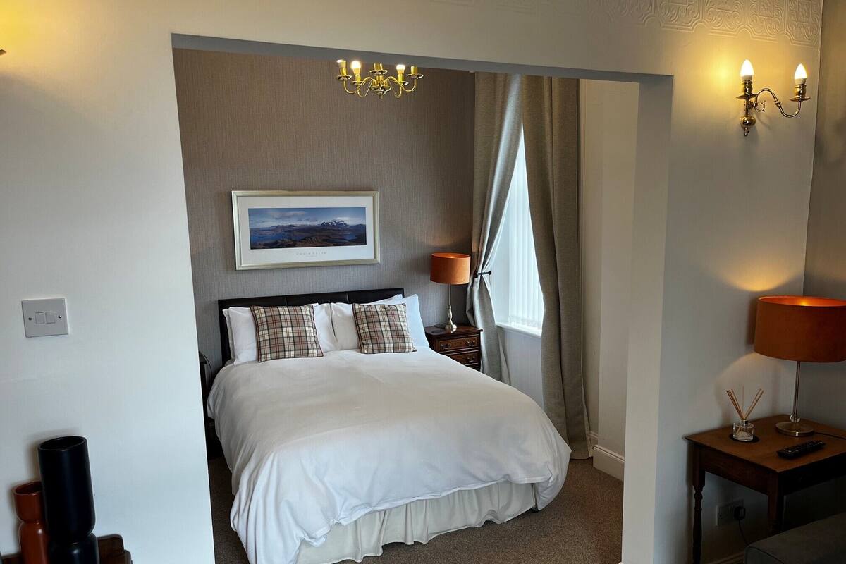 Un dormitorio ordenado con cama, mesita de noche, lámpara, un cuadro en la pared y candelabro.