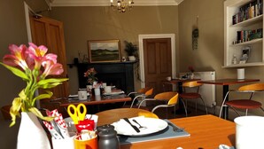 Un coin repas avec une table en bois dressée pour deux personnes, des chaises, un vase avec des fleurs, une cheminée et une bibliothèque.