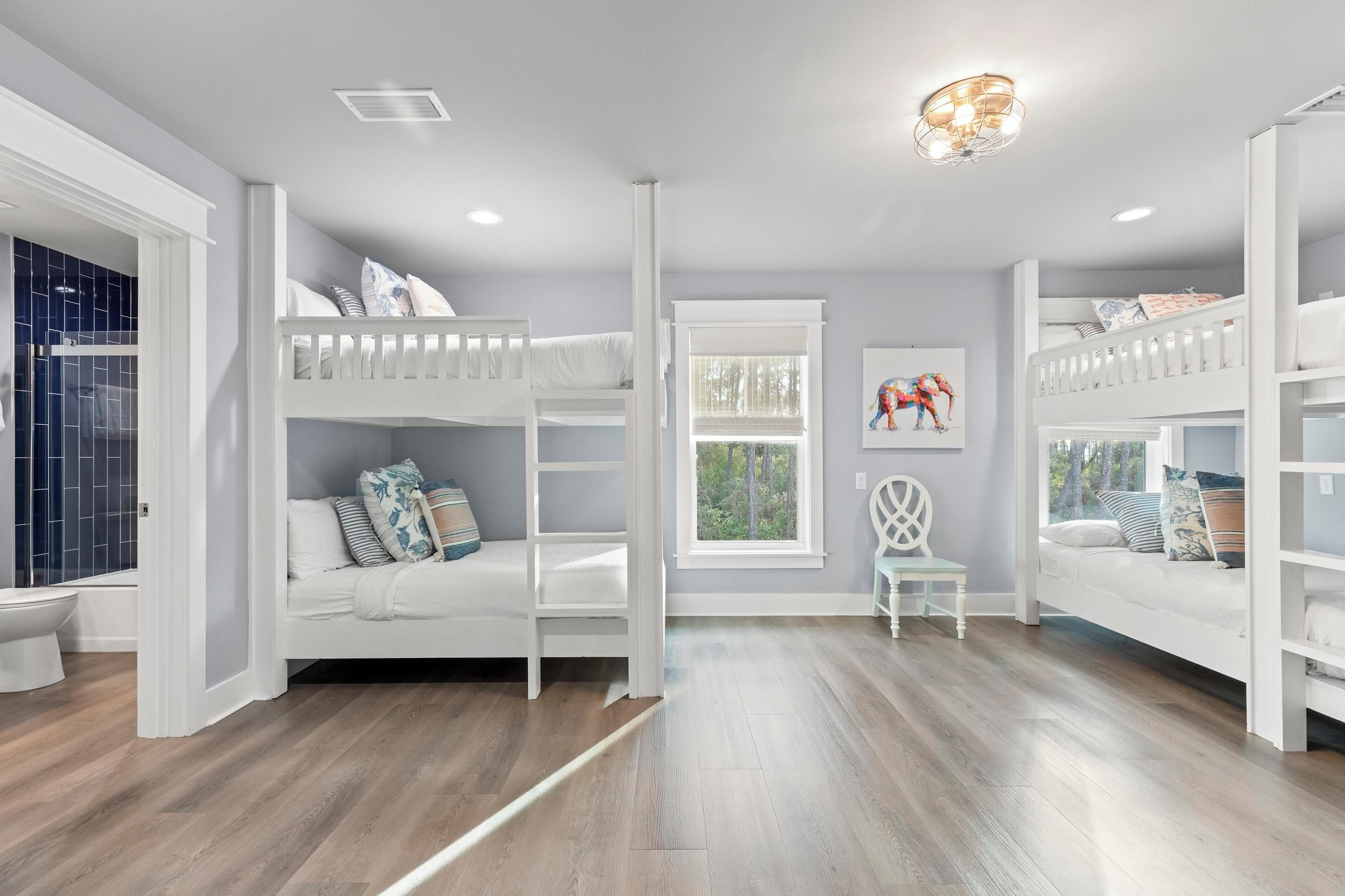 A child’s room with bunk beds, a window, and a white chair.