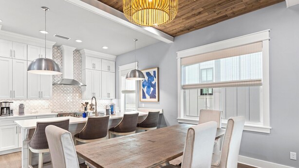 A modern kitchen with white cabinets, a wooden dining table, and pendant lighting. - 30A Pet Friendly House - Scissortail  (Panama City Beach)