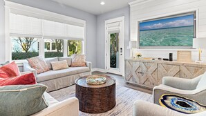 A modern living room with a large TV, comfortable seating, and a view of the outdoors. - 30A Pet Friendly House - Scissortail  (Panama City Beach)