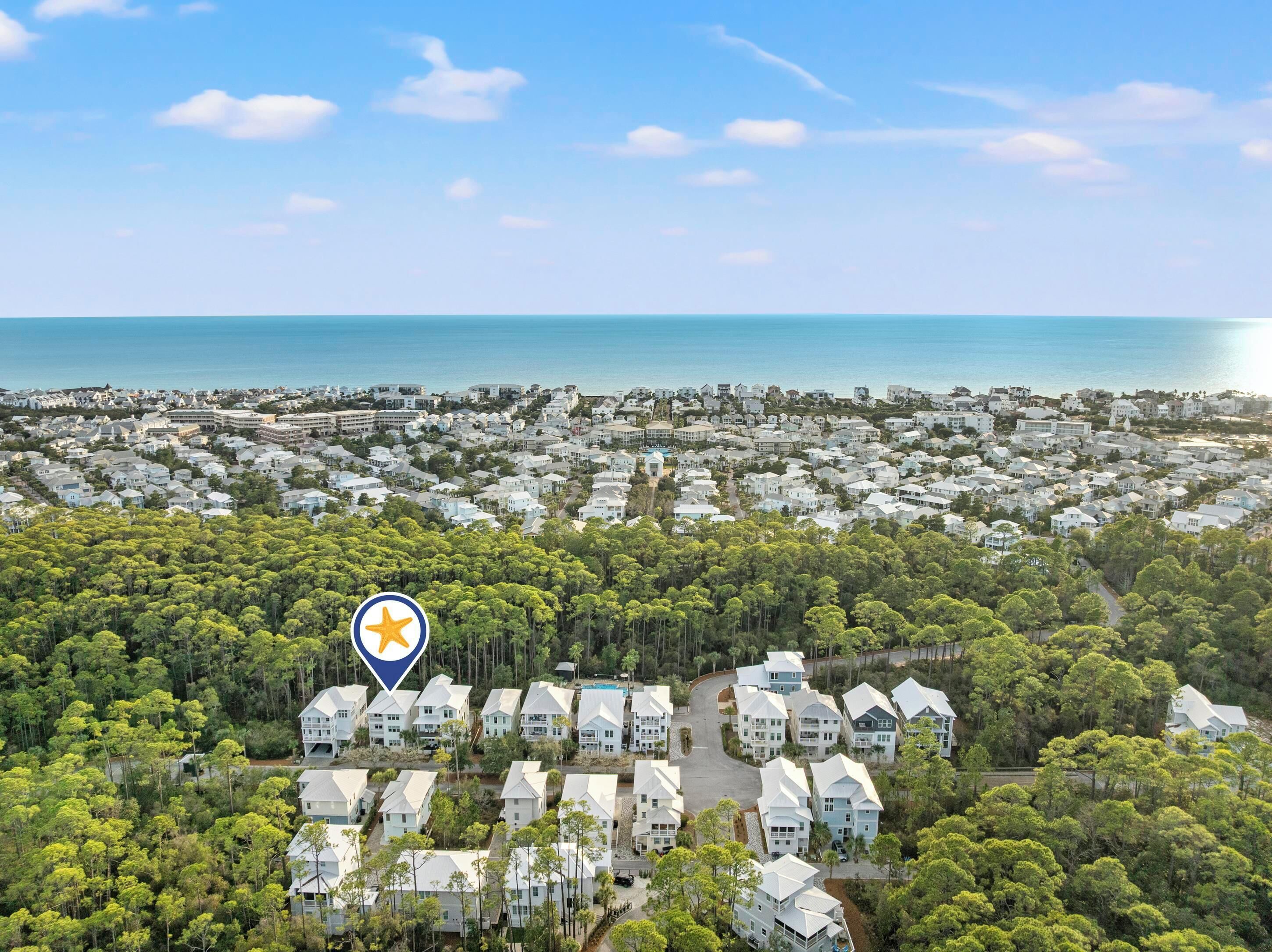 A coastal residential area with a dense cluster of houses surrounded by trees and a view of the sea.