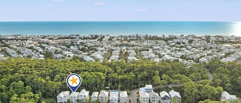 A coastal residential area with a dense cluster of houses surrounded by trees and a view of the sea.