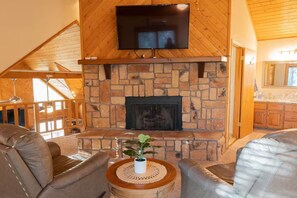 A cozy living room with a stone fireplace, leather sofas, and a flat-screen TV mounted above the fireplace. - Circle C on Timberline (Ruidoso)