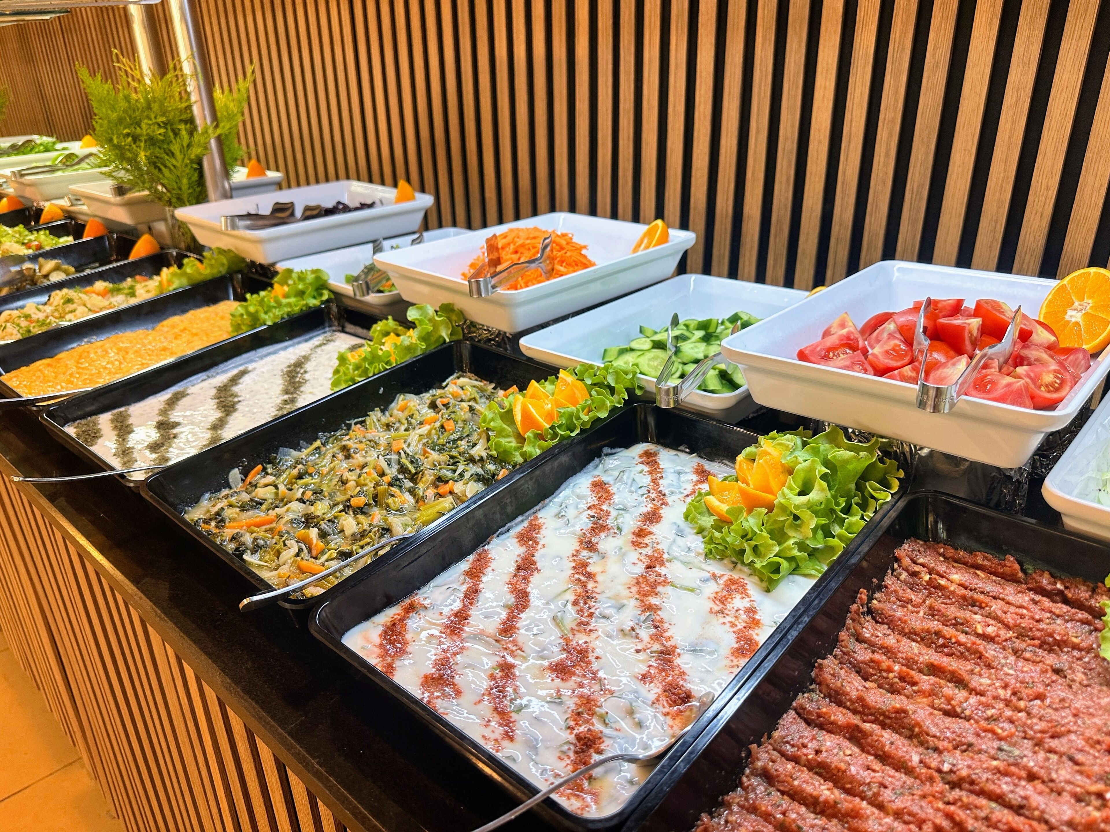 A buffet with various food options including salads, meats, and a creamy dish with a red spice topping.