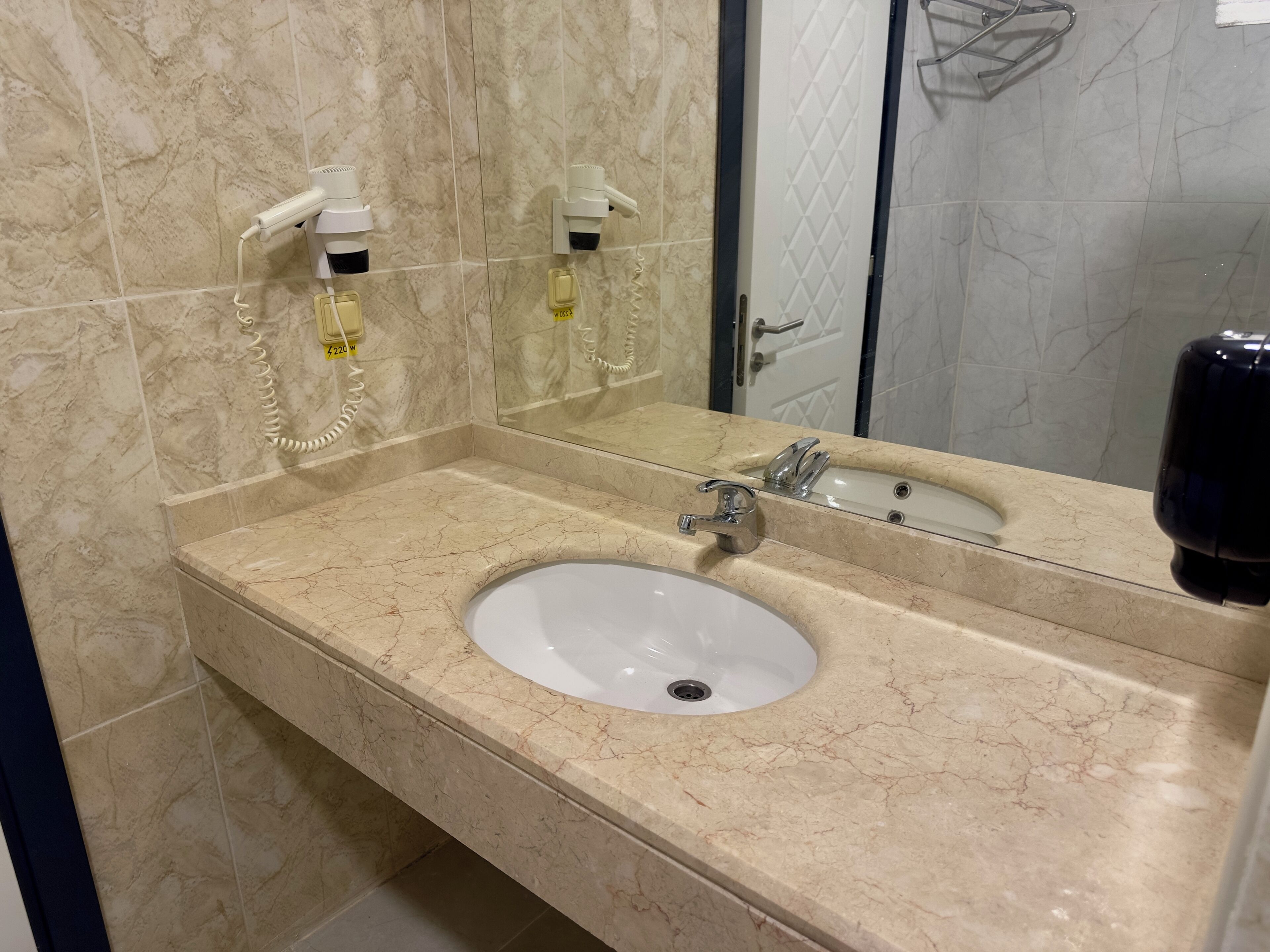 Un baño con lavamanos de mármol, un espejo y dispensador de toallas.