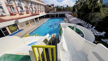 Una piscina con toboganes y sillas de descanso, rodeada por un edificio con balcones.