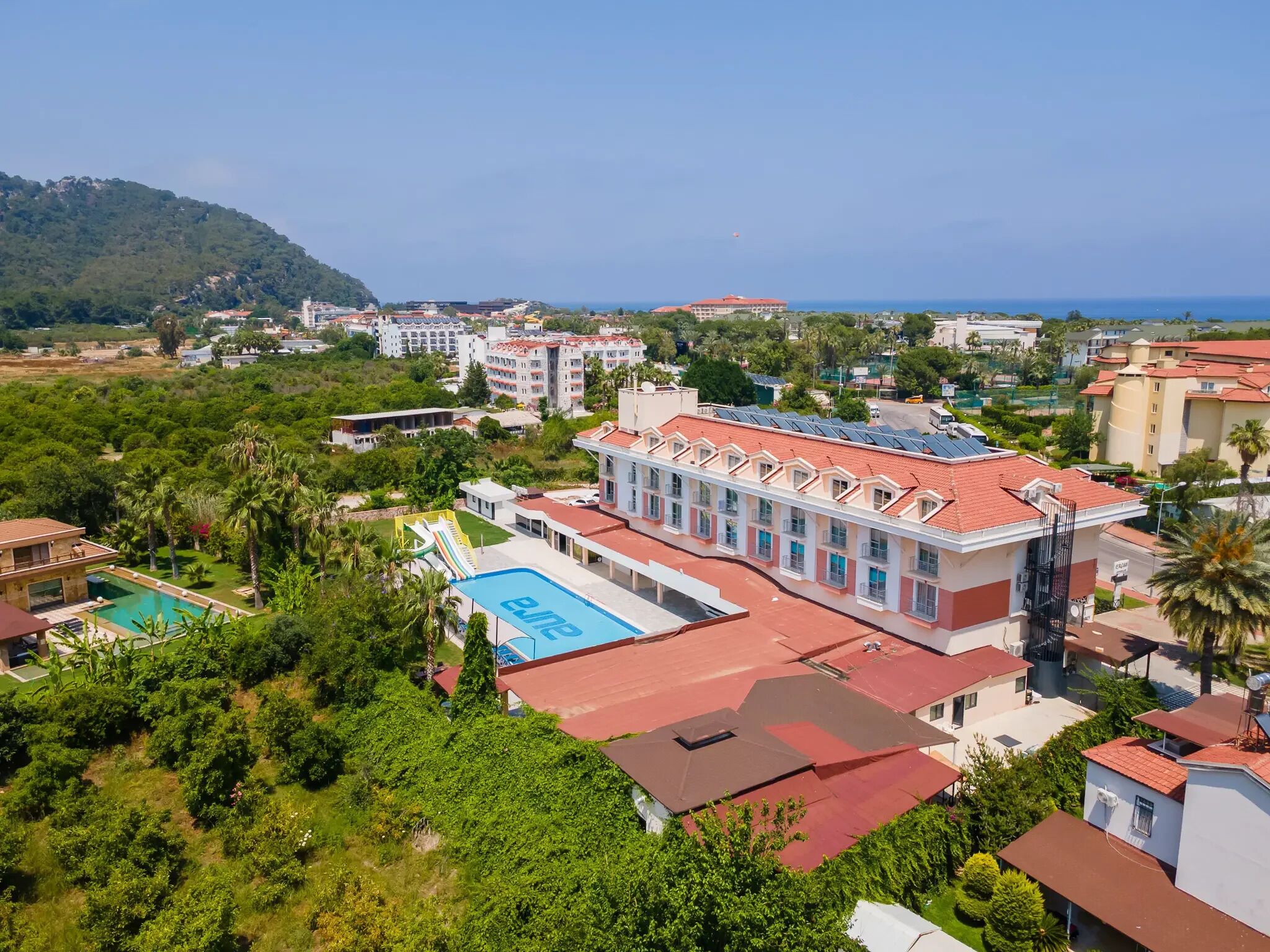 A hotel with a swimming pool, multiple buildings, and a hilly landscape in the background.