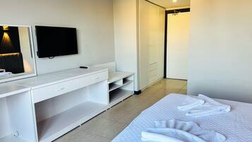 A hotel room with a bed, a desk with a flat-screen TV, a wardrobe, and a bathroom visible through an open door.