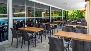 An outdoor dining area with tables and chairs, large windows, and a view of a swimming pool. - Pera Aura Resort Hotel & Spa - All Inclusive (Kemer)