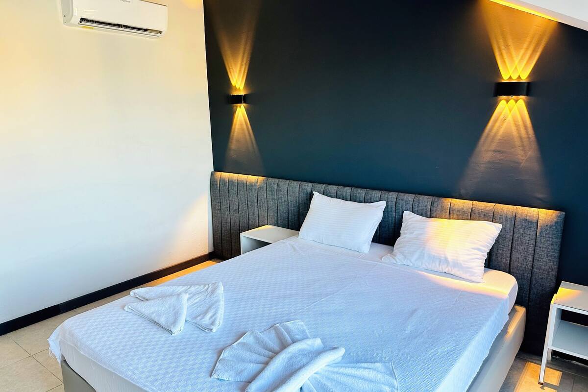 Une chambre d’hôtel comprenant un lit, deux tables de chevet, un appareil de climatisation et des lampes fixées au mur.