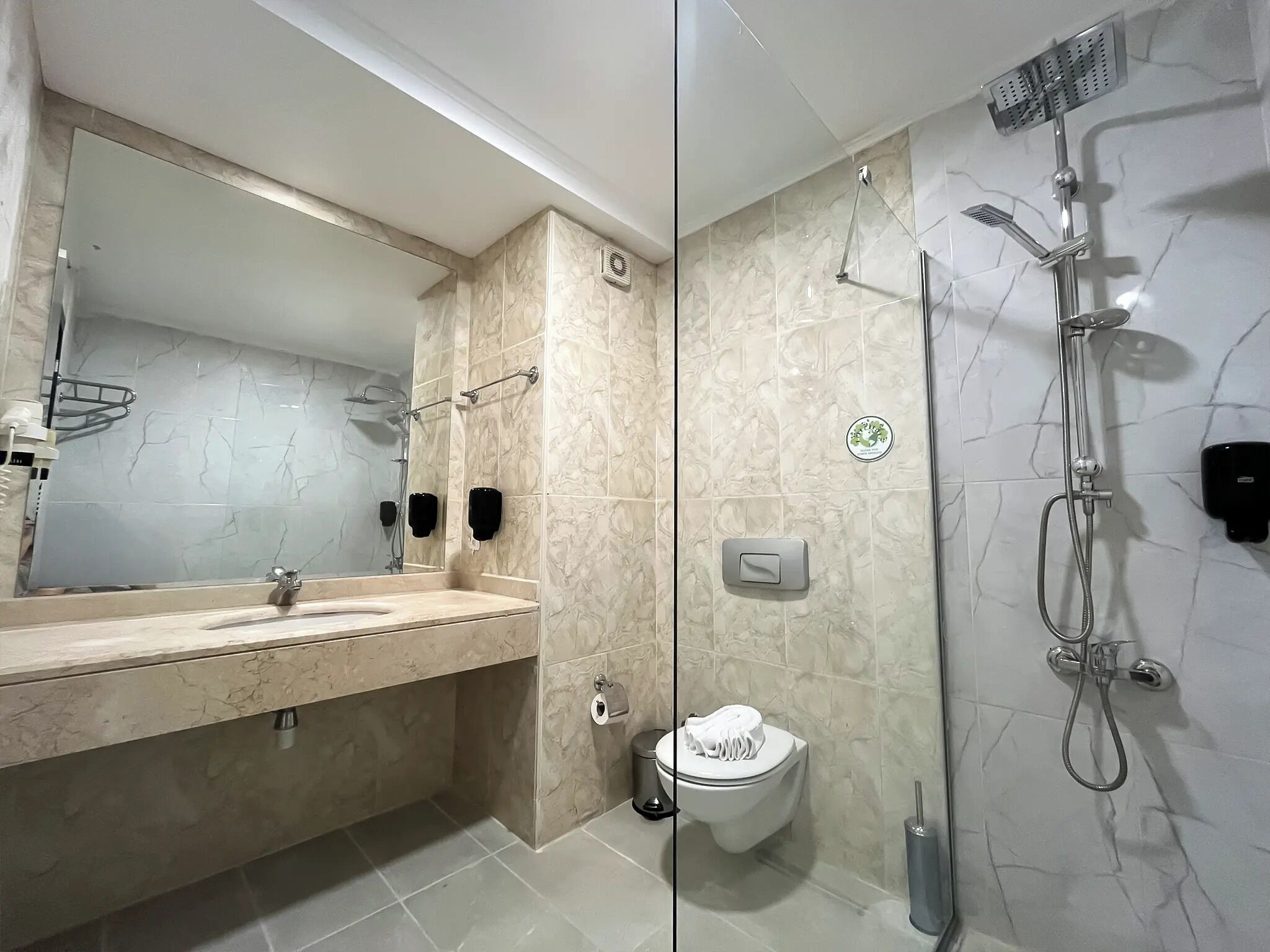 Un bagno moderno con un mobile vanitario in marmo, uno specchio grande, una doccia con soffione a mano e un water.