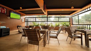 A restaurant with wicker furniture, a TV screen, and large windows. - Serenity Sports Oasis (Kampala)