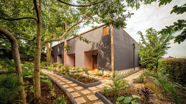 A modern building with a grey exterior, surrounded by lush greenery and a stone pathway leading to the entrance. - Serenity Sports Oasis (Kampala)