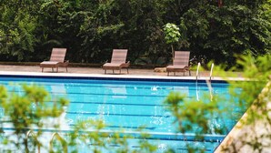 A swimming pool with three lounge chairs and a stone wall in the background. - Serenity Sports Oasis (Kampala)