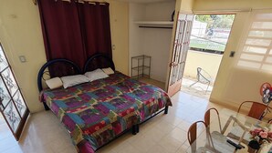 A bedroom with a bed, a desk with chairs, a small table with a vase, and a window with curtains. - Limestone House Apartment (Mérida)