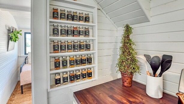 Een keuken met witte houten wanden, een houten aanrecht en een plank met kruidenpotjes.