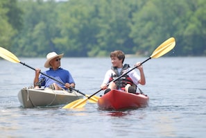 Deux personnes pratiquent le kayak sur un lac paisible, avec une végétation luxuriante en arrière-plan.