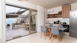 Cozinha moderna com porta de vidro para uma varanda, área de refeições com cadeiras e vista para o mar.