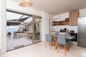 Eine moderne Küche mit Glastür zu einem Balkon, einem Essbereich mit Stühlen und Blick auf das Meer.
